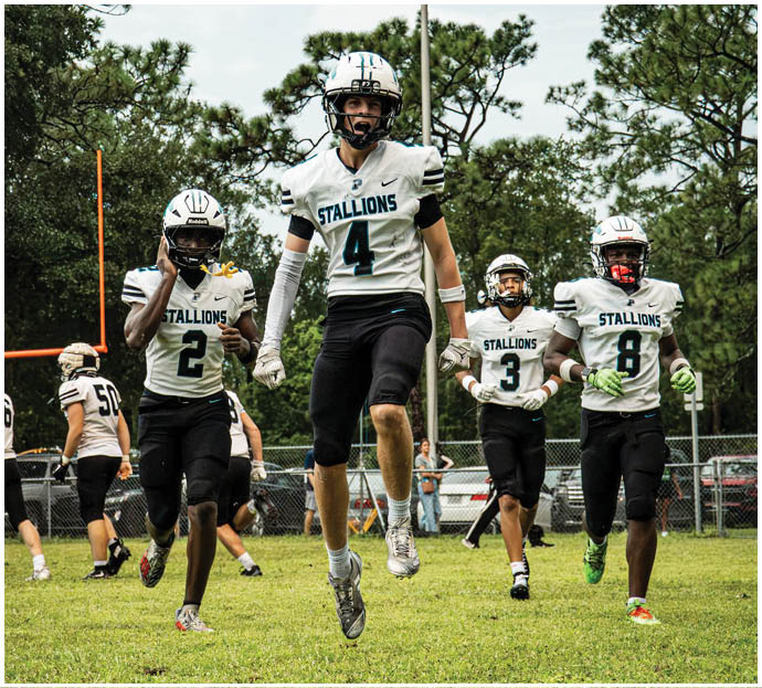 Three football players in blue and white uniforms running on a field. Description generated by AI