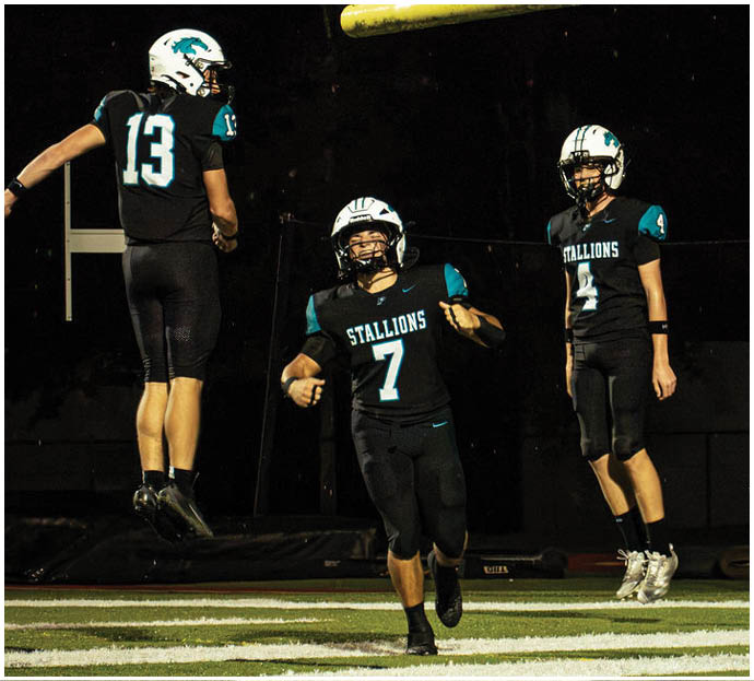 Three football players in blue and white uniforms running on a field. Description generated by AI