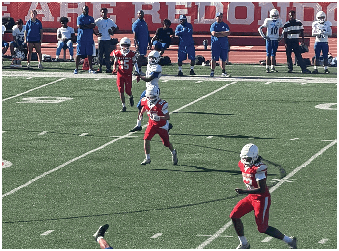 Three football players in blue and white uniforms running on a field. Description generated by AI