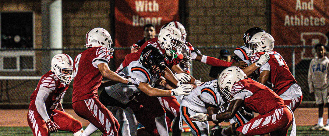 Four people wearing black sports jerseys with “VISTA" on them stand closely together in front of a large crowd, with one person raising an arm in celebration. Description generated by AI