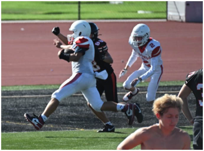Three football players in blue and white uniforms running on a field. Description generated by AI