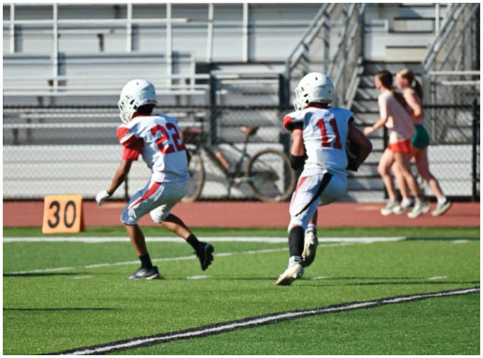 Three football players in blue and white uniforms running on a field. Description generated by AI