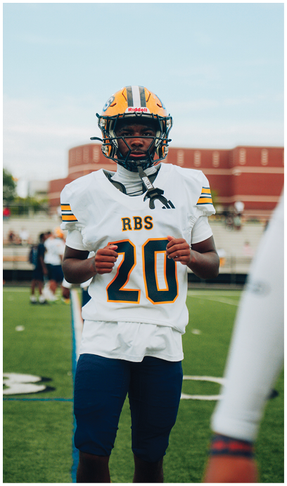 A person wearing a football uniform with the number 20 and a helmet stands on a football field with a blurred stadium background. Description generated by AI