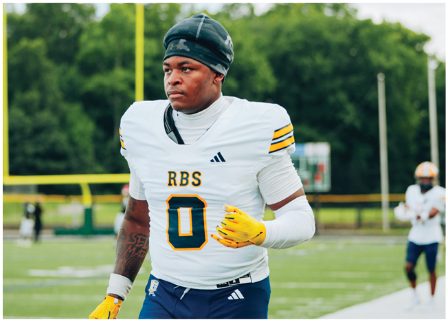 A person wearing a white football jersey with the number zero and yellow gloves is walking on a football field with another person in the background. Description generated by AI