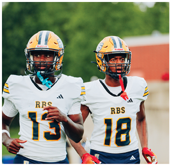 Two adults wearing football helmets and uniforms with numbers 13 and 18 are walking together on a sports field. Description generated by AI