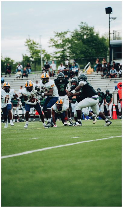 Several people wearing football uniforms are actively engaged in a play on a grassy field with spectators in the background. Description generated by AI