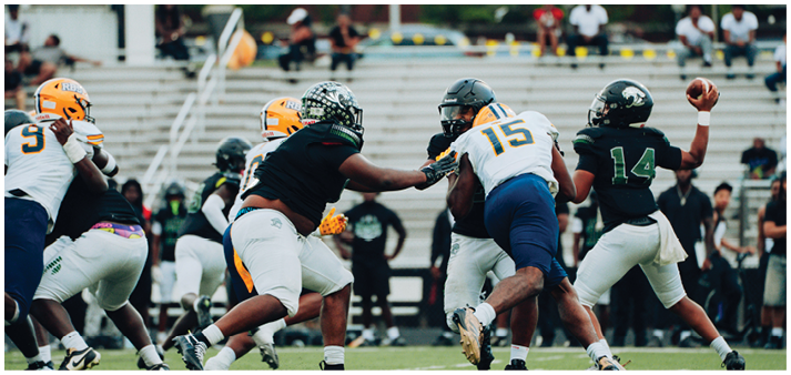 A group of people in football uniforms are actively playing on a field with one person preparing to throw a football while others attempt to block or tackle. Description generated by AI