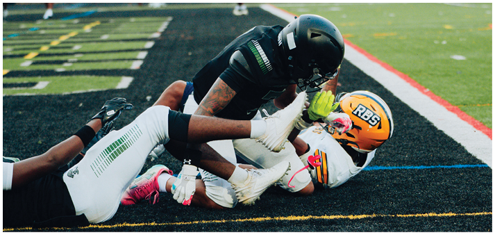 Two people in football gear are on the ground near the end zone with a football loose nearby on the field. Description generated by AI