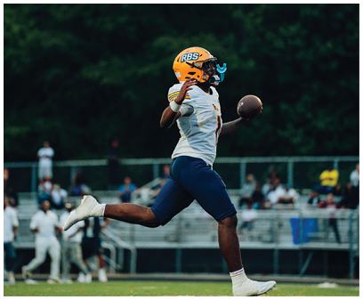 A person wearing a yellow helmet and sports uniform is running on a field while holding a football. Description generated by AI