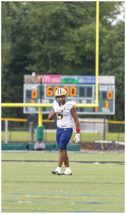 A person wearing a football uniform stands on a field with a scoreboard and goalpost visible in the background. Description generated by AI