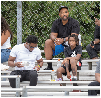 People sitting on bleachers outdoors with one person eating from a bowl and others sitting or standing nearby, dressed casually. Description generated by AI