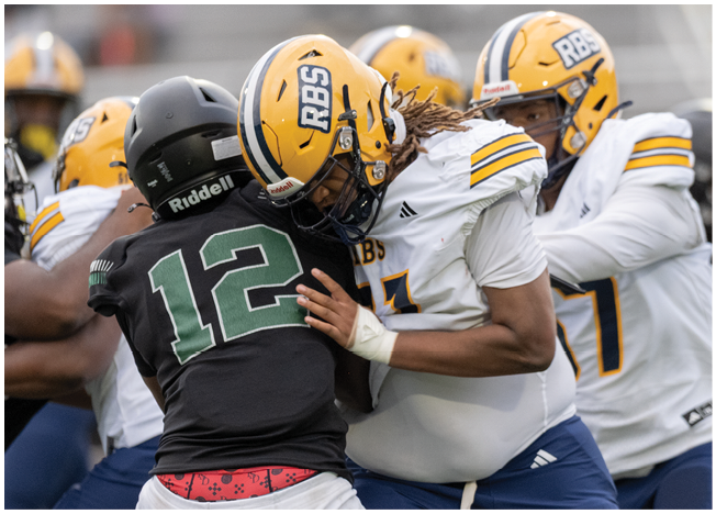 Two people in football uniforms are engaged in a tackle during a game, with one wearing a yellow helmet and white jersey and the other in a black helmet and black jersey. Description generated by AI