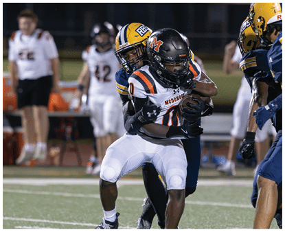 Two people in football uniforms are engaged in a tackle during a nighttime game on a field. Description generated by AI
