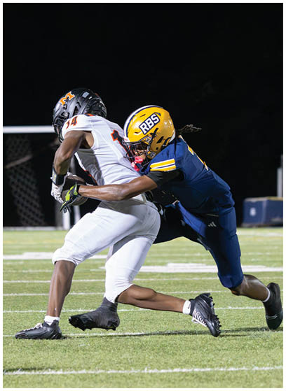Two people in football uniforms are engaged in a tackle on a well-lit field at night. Description generated by AI