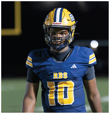 A person wearing a blue football jersey with yellow and white stripes on the shoulders and the number 10 with the letters RBS on the front stands on a field. Description generated by AI