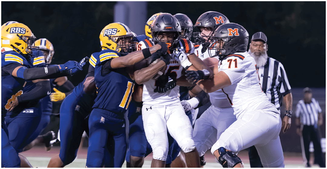 People wearing football uniforms and cleats are engaged in a close physical play on a field. Description generated by AI