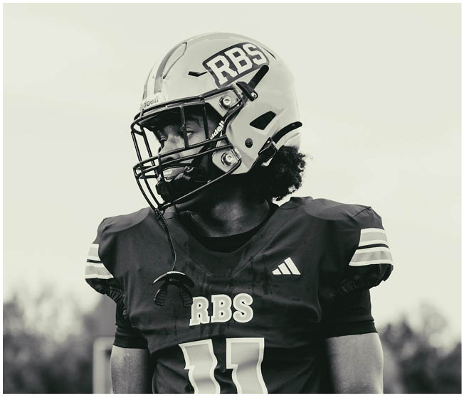 A person wearing a football helmet and jersey with the number 11 and the letters RBS is standing outdoors with a blurred background. Description generated by AI