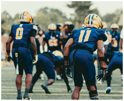 A group of people wearing blue and yellow football uniforms are gathered on a field, preparing for a play. Description generated by AI