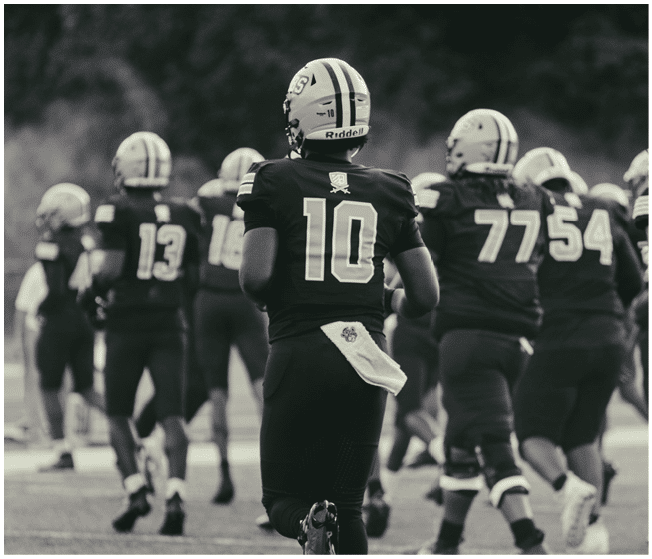 Several people in football uniforms are walking or jogging on a field with one person wearing number 10 prominently in the center. Description generated by AI