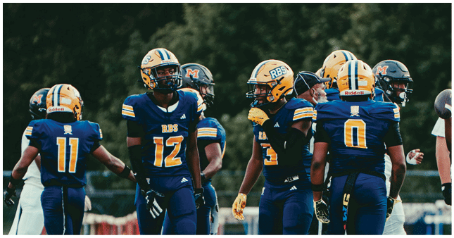 A group of people wearing blue and yellow football uniforms and helmets are gathered on a field with trees in the background. Description generated by AI