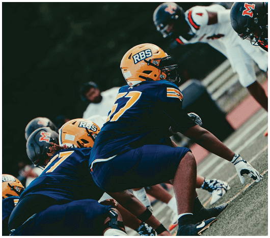 People in football uniforms are lined up on a field preparing for a play during a game. Description generated by AI