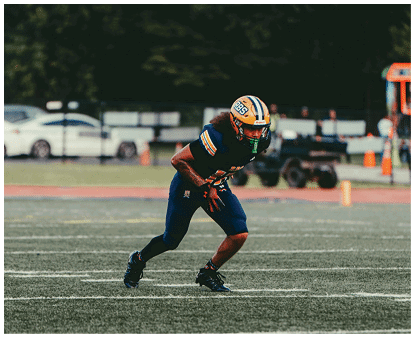 A person wearing a football helmet and uniform is bent forward on a field, appearing ready to start a play. Description generated by AI