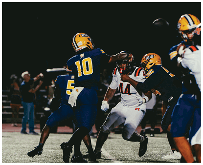 A group of people in football uniforms are actively engaged in a nighttime game with one person throwing a football. Description generated by AI