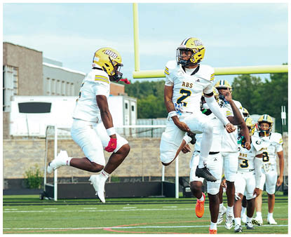 People in white and yellow football uniforms are jumping and celebrating on a green field near a goalpost. Description generated by AI