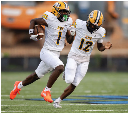Two people in white football uniforms with numbers 1 and 12 are running on a grassy field during a game. Description generated by AI