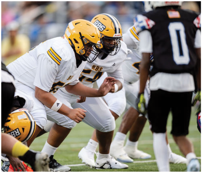 Several people in white and yellow football uniforms are crouched in a ready position on a football field facing opponents in black uniforms. Description generated by AI