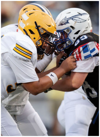 Two people in football uniforms and helmets are engaged in a close physical confrontation on the field during a game. Description generated by AI