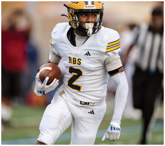 A person wearing a white football uniform with the number 2 and a yellow helmet is running while holding a football on a field. Description generated by AI
