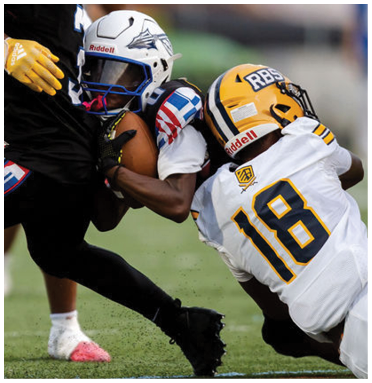 Two people in football gear are tackling a third person wearing black athletic clothing on a grassy field during a game. Description generated by AI