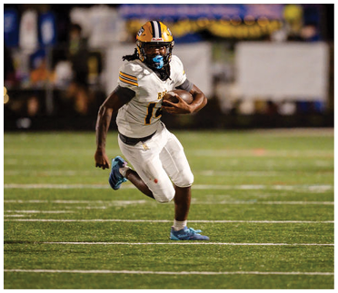 A person wearing a white football uniform with a yellow helmet is running on a football field while holding a football. Description generated by AI