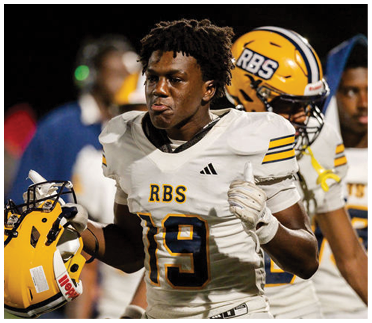 A person in a white football uniform with the number 19 and the letters RBS is holding a yellow helmet and appears focused during a game. Description generated by AI