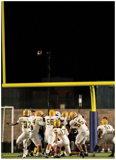 A football is captured mid-air against a dark night sky with a goalpost faintly visible in the background. Description generated by AI