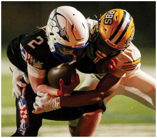 Two football players in helmets and uniforms are engaged in a tackle during a game, with one player holding the ball tightly. Description generated by AI
