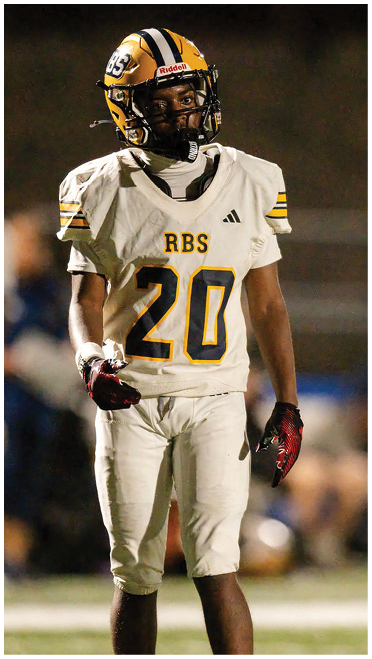 A person wearing a white football uniform with the number 20 and a yellow helmet stands on a field during a game. Description generated by AI