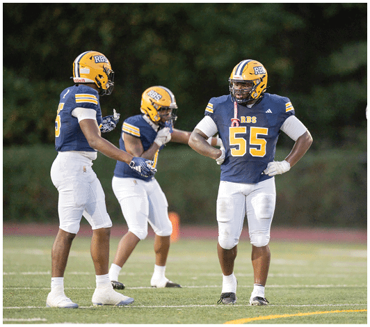 People wearing blue and yellow football jerseys with “RBS" on them stand closely together with serious expressions. Description generated by AI