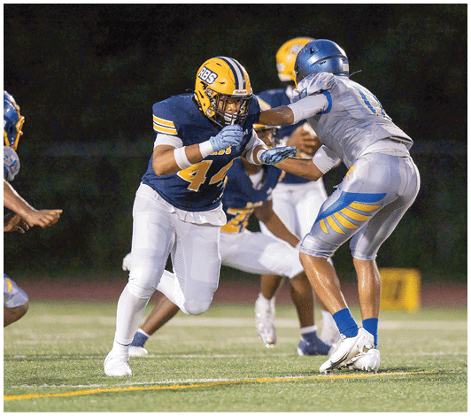 A person wearing a blue and yellow football uniform with the number 57 is running on a field with other players blurred in the background. Description generated by AI