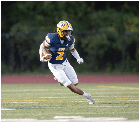 A person wearing a blue and yellow football uniform with the number 57 is running on a field with other players blurred in the background. Description generated by AI