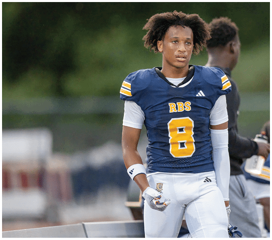 A person wearing a blue and yellow football uniform with the number 57 is running on a field with other players blurred in the background. Description generated by AI