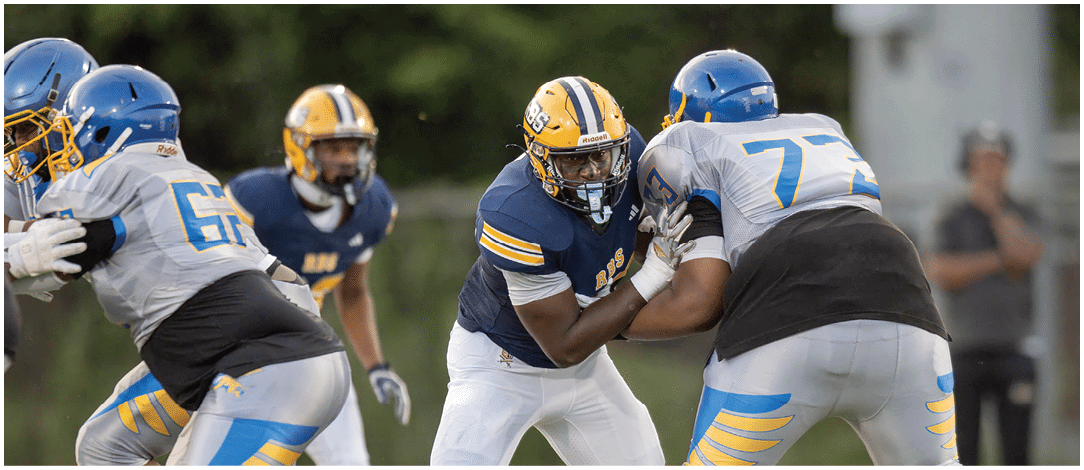 A person wearing a blue and yellow football uniform with the number 57 is running on a field with other players blurred in the background. Description generated by AI