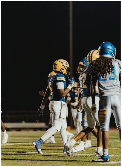 Several people wearing football uniforms and helmets are standing on a field at night. Description generated by AI