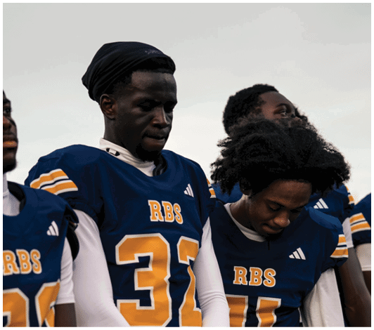 People wearing blue and yellow football jerseys with “RBS" on them stand closely together with serious expressions. Description generated by AI