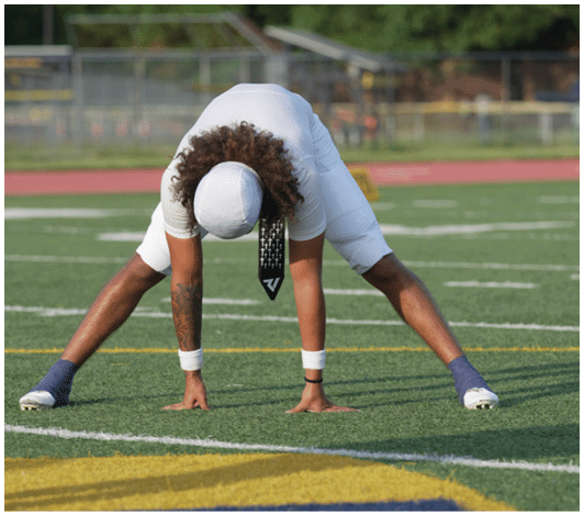 Three people wearing athletic shoes stand on a grassy sports field with a blurred background. Description generated by AI