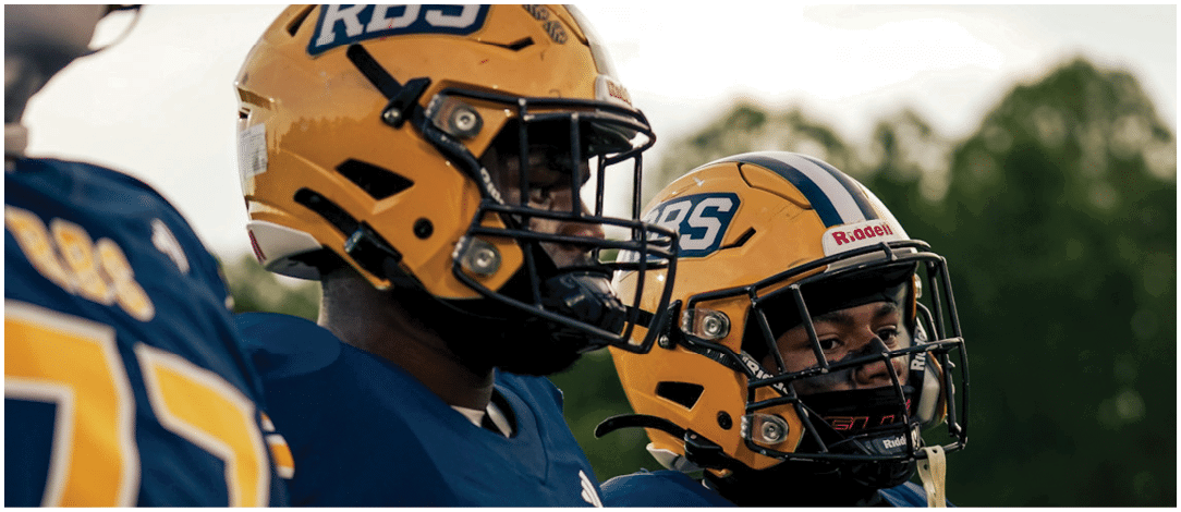 People wearing football helmets with RBS logos are seen outdoors against a cloudy sky. Description generated by AI