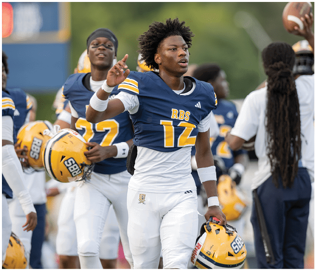A person wearing white sports pants is holding a yellow football helmet with a logo and the number 58 on it while standing among other people. Description generated by AI