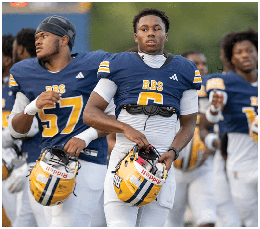 People wearing white sports uniforms hold yellow and black football helmets while standing in a line. Description generated by AI