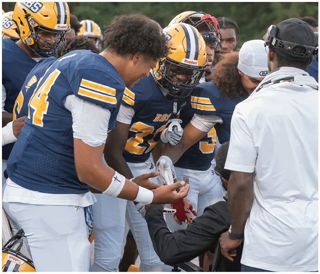 A group of people wearing blue and yellow football uniforms are gathered closely together, appearing to celebrate or share a moment of excitement. Description generated by AI